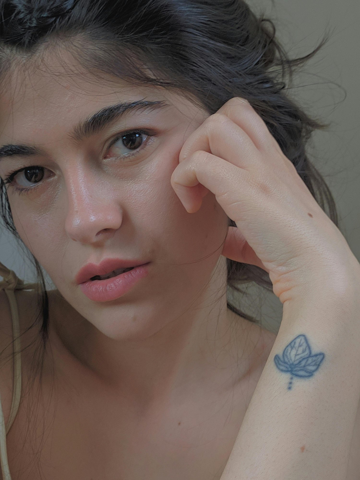 A dark haired woman looking defeated of her human rights holding her hand up to her face with a small tattoo on her wrist.